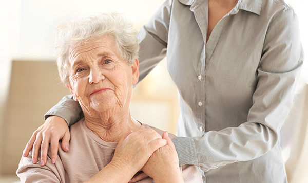Elderly woman smiling, young person comforting her. Warm interaction.